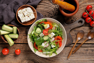 Bowl of fresh vegetable salad with cucumber and feta cheese on wooden background