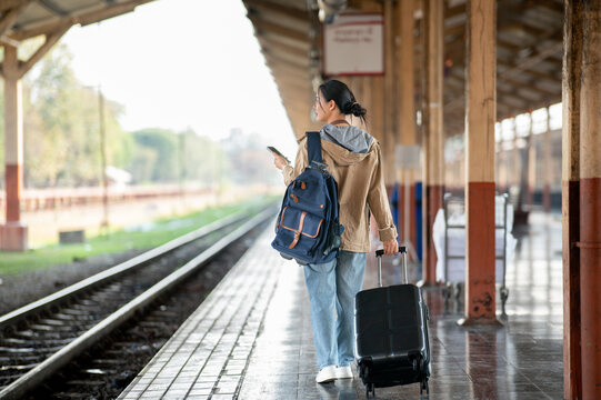 Back view of an asian woman walking away with luggage in an empty train station or railway station..