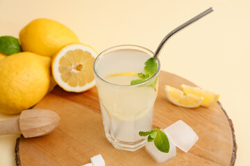 Glass of fresh lemonade with mint and wooden juicer on yellow background