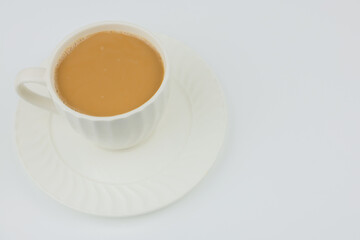 A white mug of coffee stands on a white saucer, black aromatic coffee with milk and foam around the edges is poured into the mug on a white background with space for text. The concept of black coffee