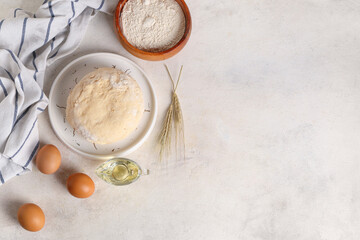 Plate with fresh raw dough, eggs, wheat and bowl of flour on white background
