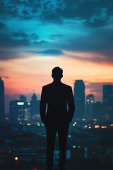 Fototapeta premium Silhouette of a businessman standing confidently in front of a city skyline at sunset.