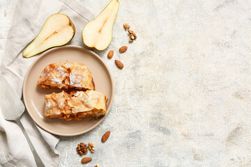 Plate with pieces of tasty pear strudel, fresh cut fruit, nuts and spatula on grey grunge background
