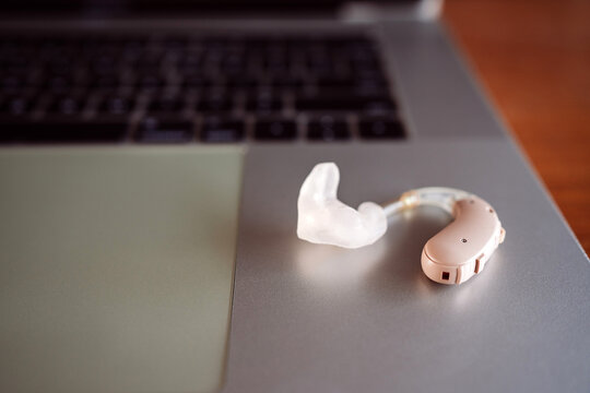 A modern hearing aid with a custom ear mold rests on a laptop, symbolizing the intersection of technology and accessibility. Concept of hearing loss, assistive devices, and digital inclusion.