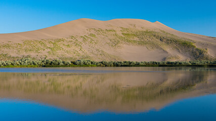 A striking image of a sweeping sand dune mirrored in still waters, showcasing the dynamic contrast...