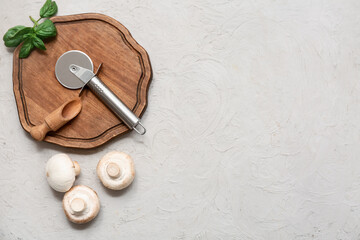 Wooden board with stainless steel pizza cutter and mushrooms on light background