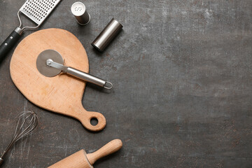 Set of kitchen utensils with stainless steel pizza cutter and spices on dark background