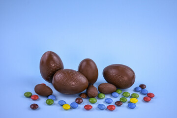 Festive Easter composition with chocolate eggs of different sizes and multi-colored candies on a light blue background.