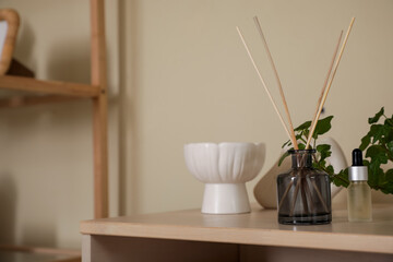 Aroma reed diffuser with essential oil, decor and houseplant on chest of drawers in room. Closeup