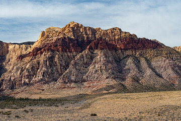 Majestic mountains painted in vibrant colors rise against a dramatic, soft cloud cover, depicting the extraordinary beauty of geological formations in nature.