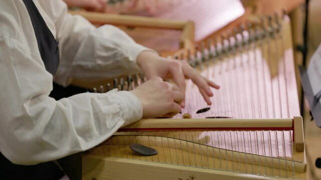 Close-up of musicians playing the kokle, a traditional Latvian string instrument, with fingers delicately plucking the strings, highlighting the craftsmanship, precision, and cultural heritage