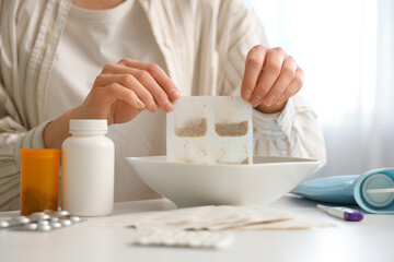 Young woman dipping mustard plaster into bowl of water at table in bedroom, closeup