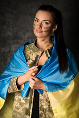 Fototapeta premium Beautiful young military woman in military uniform with camouflage makeup on her face with Ukrainian flag
