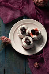 Delicious cream cakes with frozen blackberries on a plate, top view