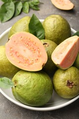 Fresh whole and cut guava fruits in bowl on grey textured table, closeup