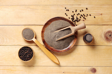 Bowl and spoon of black pepper powder with peppercorns on wooden background