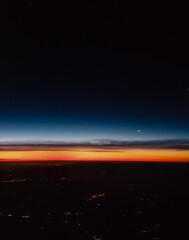 A breathtaking view of the horizon at dawn, blending deep blues, fiery oranges, and city lights from above
