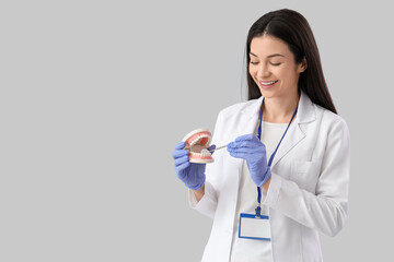 Young female dentist with tool and jaw model on light background