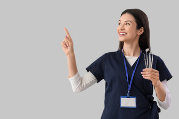 Young female dentist with tools pointing at something on light background
