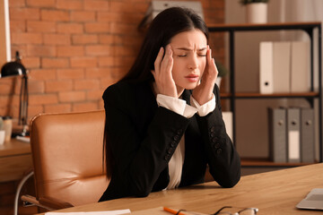 Young businesswoman suffering from headache at table in office
