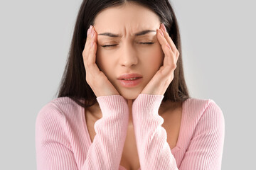 Young woman suffering from headache on light background, closeup