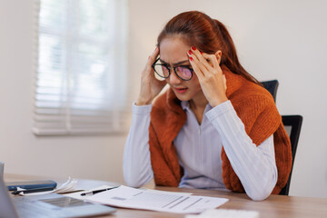 Rarissara-ThanedbovornShot of sad young asian woman overthinking while holding laptop computer and mobile phone sitting on the sofa at home
