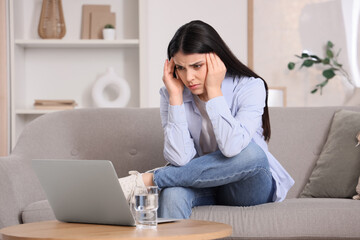 Young woman suffering from headache on sofa at home
