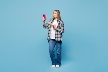Full body young woman wears checkered grey shirt casual clothes hold takeaway delivery craft paper red cup coffee to go do mobile cell phone selfie shot isolated on plain pastel light blue background.