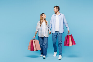 Full body young fun couple two friend family man woman wear shirt casual clothes together hold shopping paper package bags walk go isolated on plain blue background. Black Friday sale buy day concept