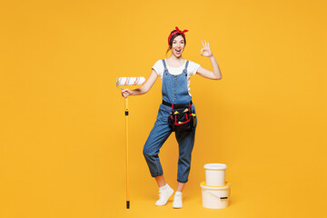 Full body young employee laborer handyman woman wear overalls belt hold paint roller bucket show ok...