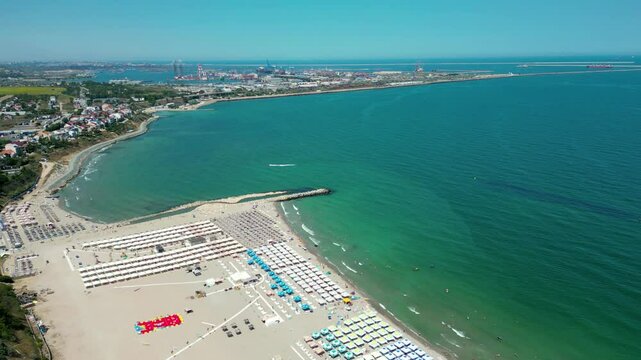 Eforie Nord Beach, Romania, aerial perspective. Famous travel destination. Season time, beach full with sunshades. People at the beaches. Turquoise water. Drone forward. Constanta port in background.