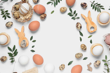 Frame made of Easter eggs with wooden bunnies and leaves on white background