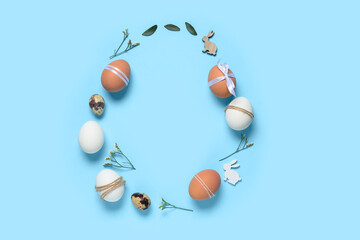 Frame made of Easter eggs, leaves, flowers and decorative bunnies on blue background