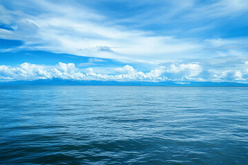 Fototapeta premium A serene view of the ocean under a bright blue sky with fluffy white clouds. The calm water reflects the sky, creating a peaceful atmosphere.