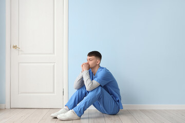 Stressed male medical intern sitting near blue wall
