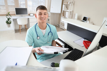 Male medical intern with papers at reception desk in clinic