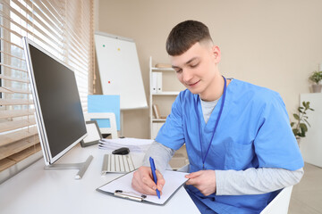Male medical intern writing on clipboard at table in clinic