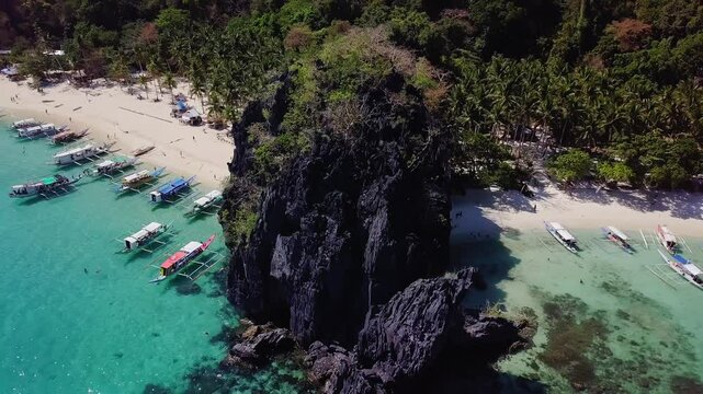 Aerial view of beautiful white sand beach, with palm trees and filipino boats in Seven Commandos beach, Palawan, Philippines. 