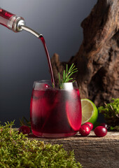Cranberry cocktail with ice, lime, and rosemary on a old wooden board.