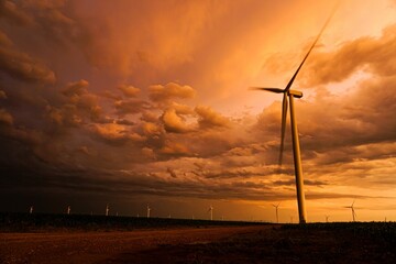 Obraz premium Dramatic sunset sky over a wind farm with turbines silhouetted against vibrant clouds