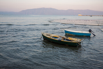 Boats quietly bobbing on calm waters at sunset near a mountainous landscape