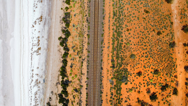 Train tracks divide a saltlake and the desert in the Australian outback, seen from above
