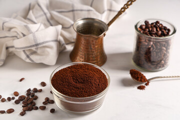 Bowl of coffee powder with beans, spoon and cezve on white background