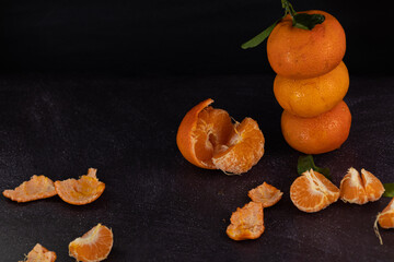 Fresh mandarins stacked on a rustic background with peeled mandarins scattered around. Dark food