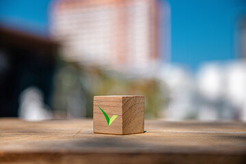 Wooden block with check mark on city bokeh background, signifying success, completion, organization...
