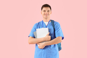 Male medical intern with notebooks and backpack on pink background