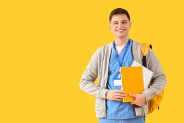Male medical intern with backpack and notebooks on yellow background
