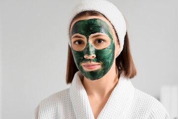 Young woman with spirulina facial mask on light background, closeup