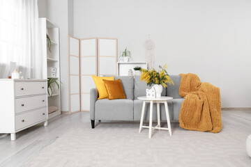 Obraz premium Interior of light living room with sofa, folding screen and mimosa flowers in vase