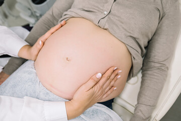 Gynecologist examining pregnant woman's belly in clinic